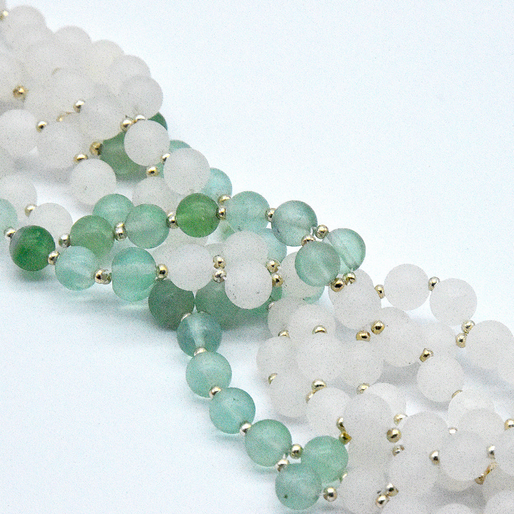Two strands of green and white beaded jewelry with gold accents on a light gray background.