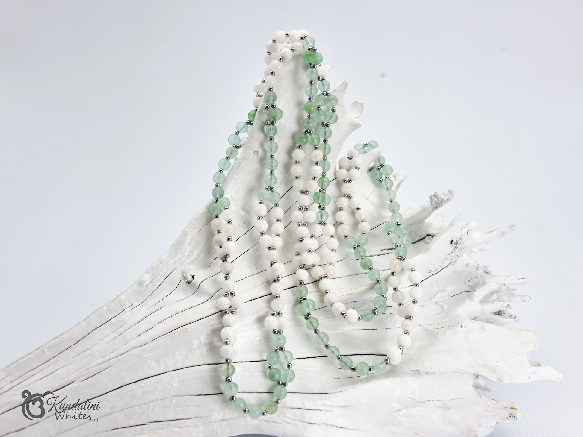 Fluorite and white agate Tantric Mala draped over a white driftwood branch against a light gray background. 