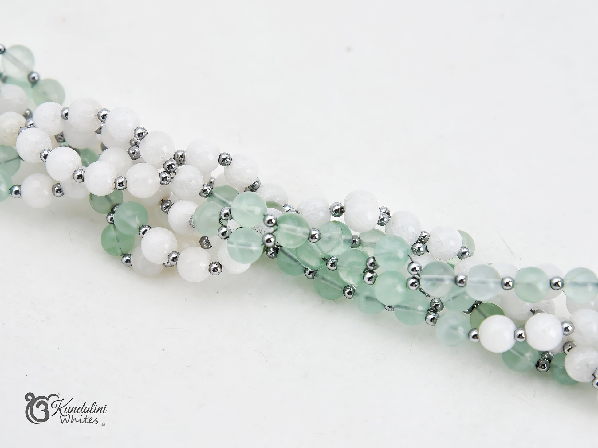A close-up of a fluorite and white agate Tantric Mala, laid diagonally on a plain white background.