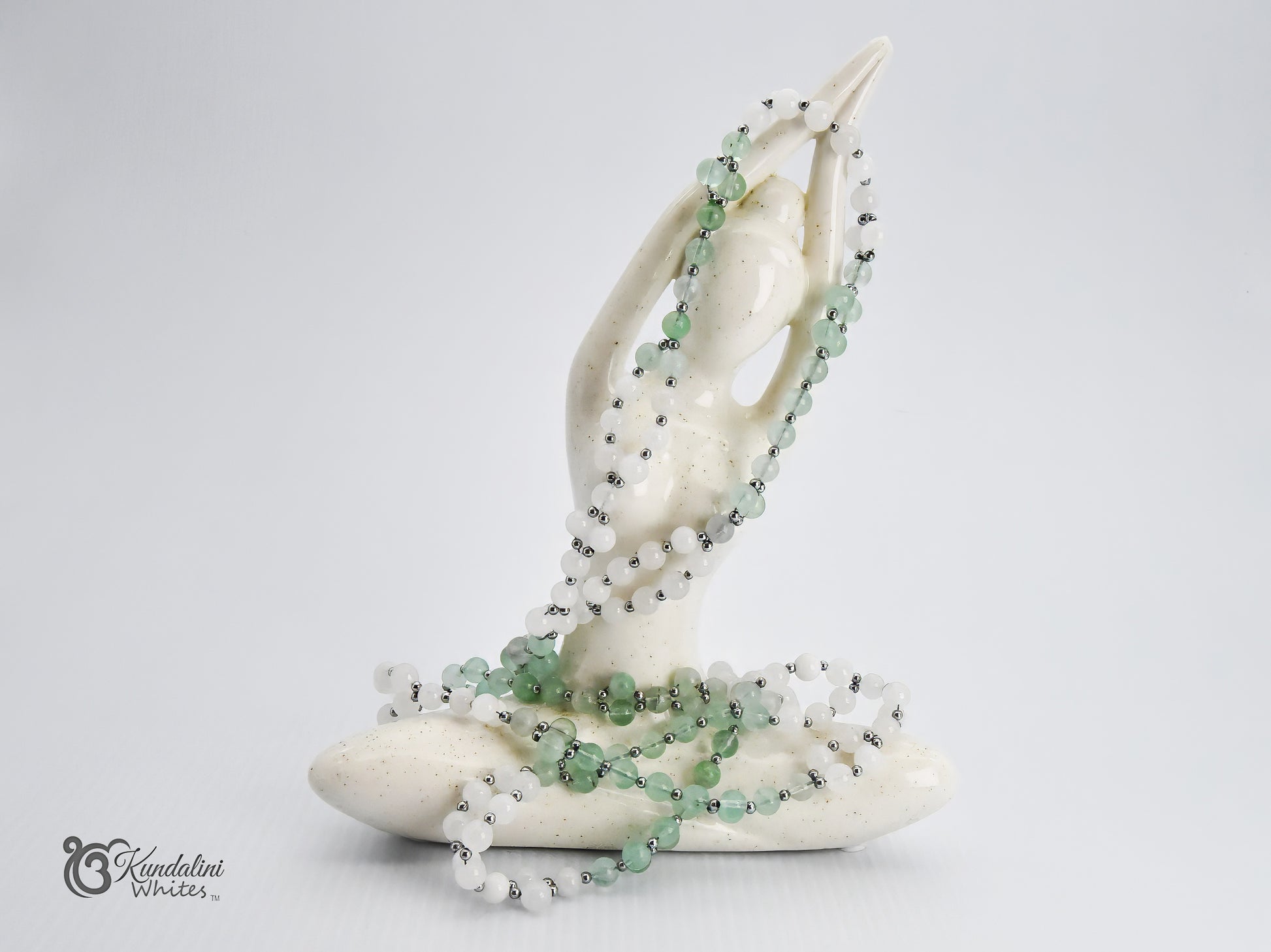 A white ceramic statue draped with a fluorite and white jade Tantric necklace, set against a plain light gray background.