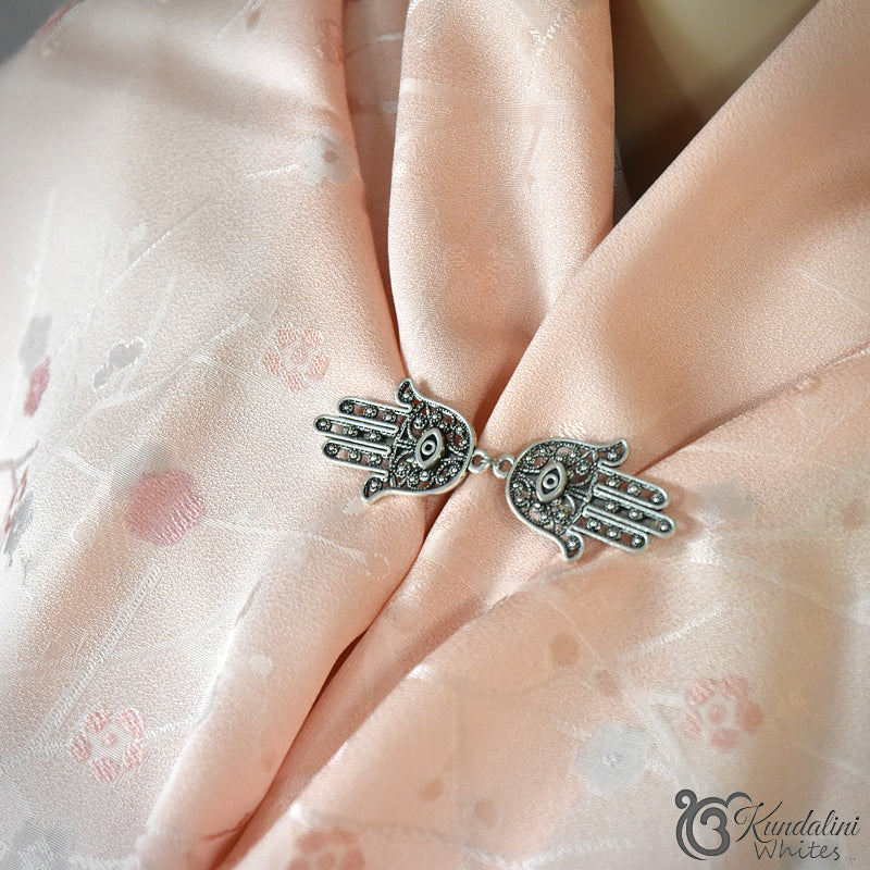 Silver Hamsa hand scarf holder on a soft pink fabric background