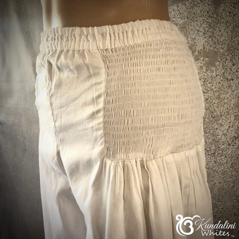 White smocked pants on a mannequin against a textured wall.