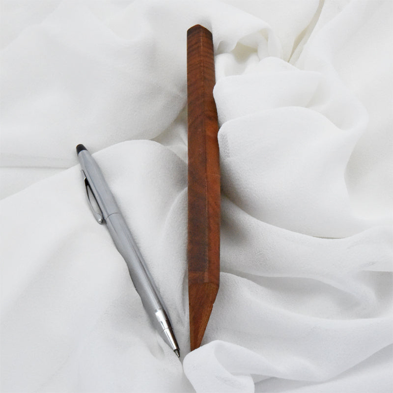 Sideview of wooden comb, with a pen for size comparison, on a white fabric background
