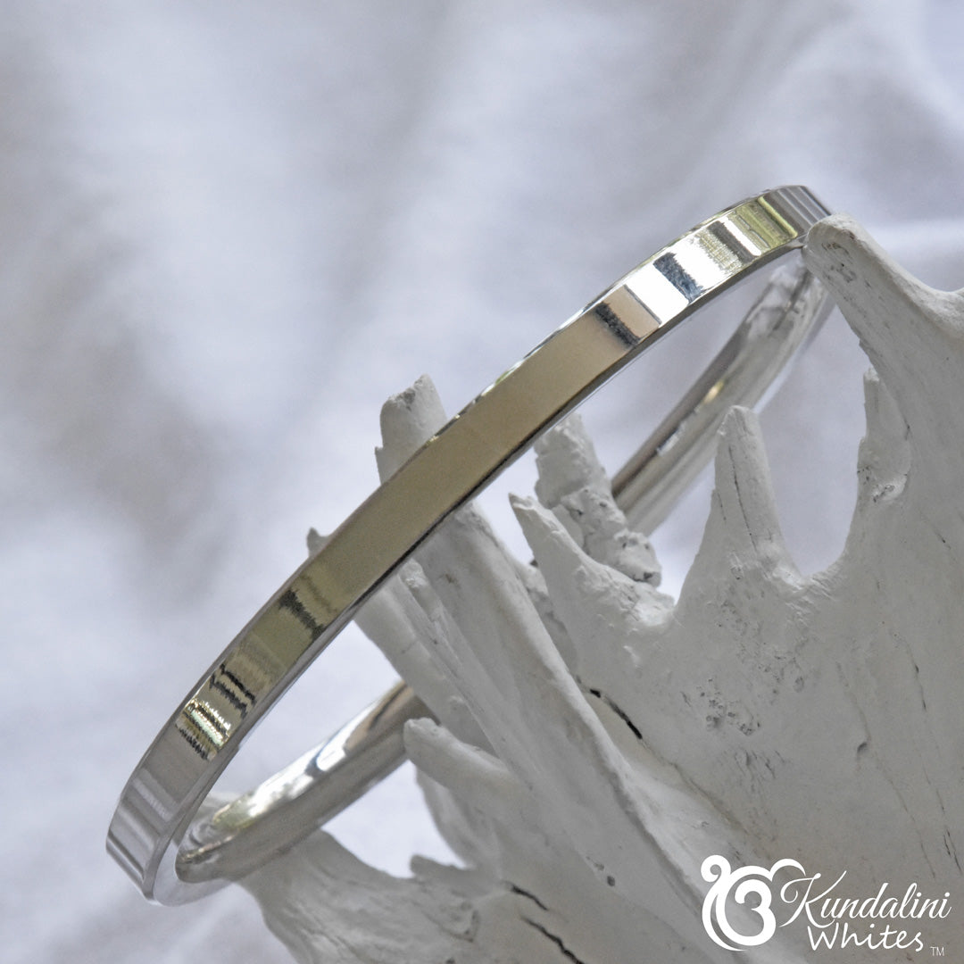 Steel Kara bracelet on a white stone surface with 'Kundalini Whites' branding.