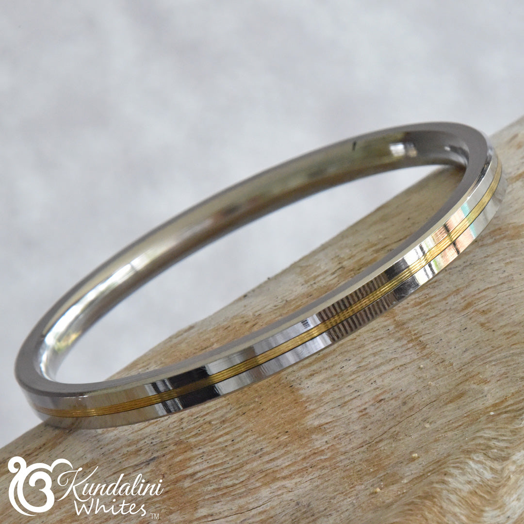 Silver and gold bangle on a wooden surface with Kandallini Whites logo.