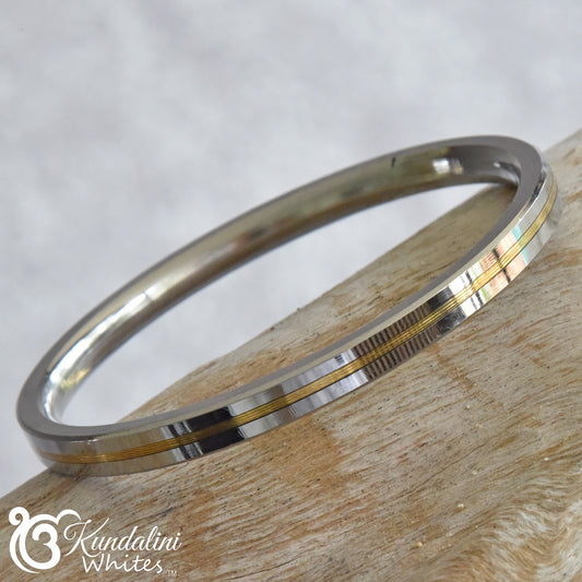 Silver and gold bangle on a wooden surface with Kandallini Whites logo.