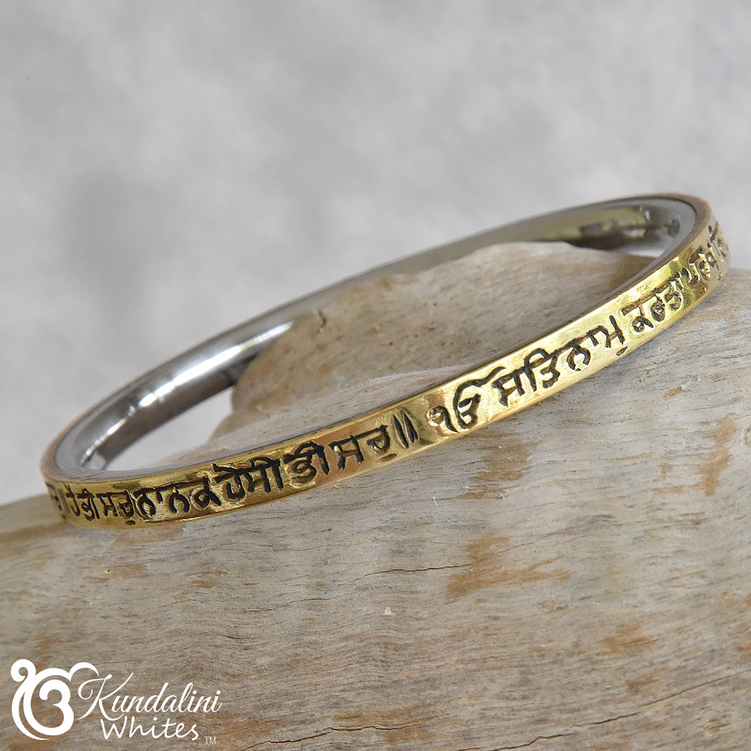 Steel and brass bracelet with engraved text on a wooden surface, featuring the brand 'Kundalini Whites'.