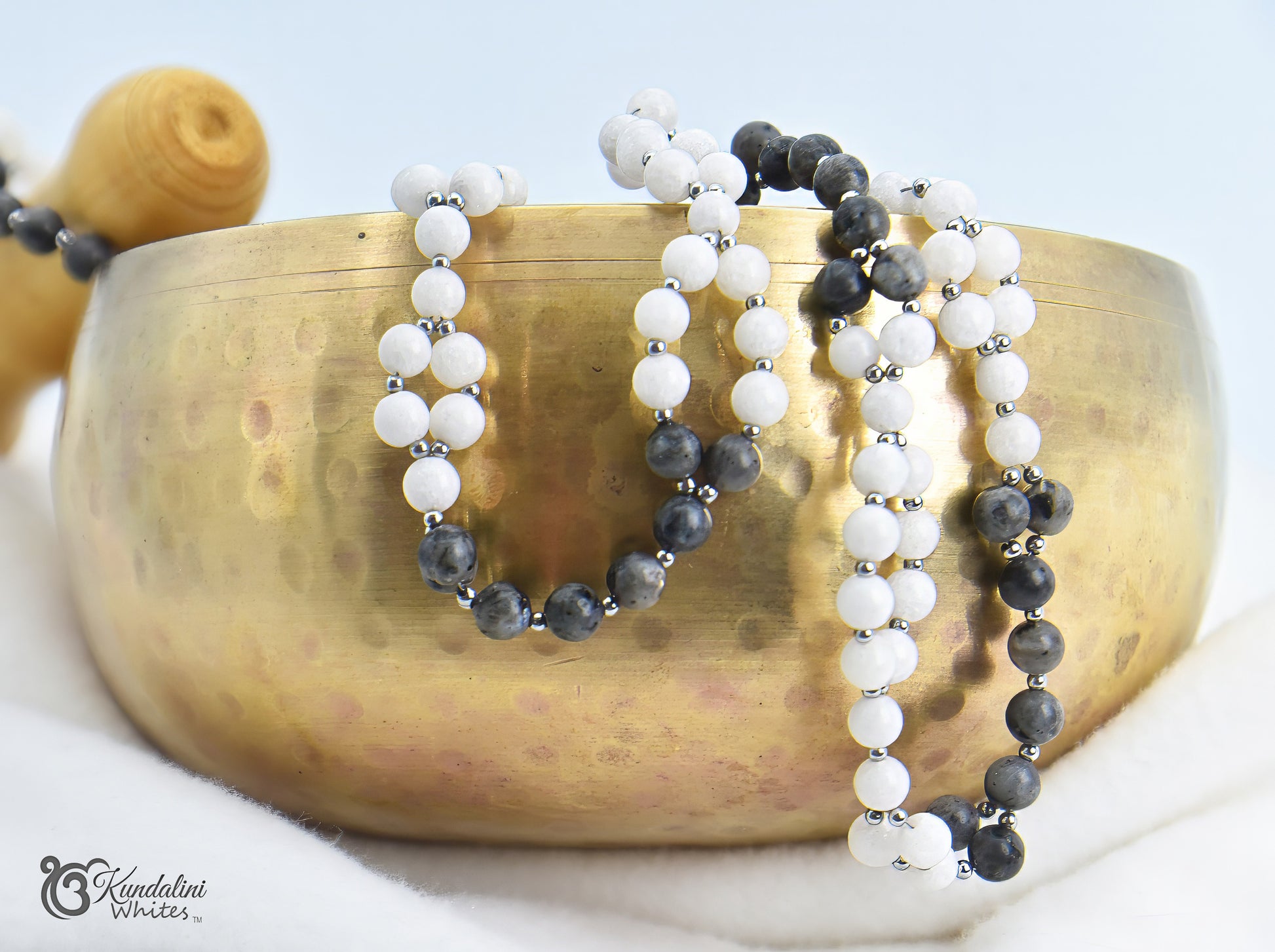 A grey and white tantric mala on a brass bowl with a white background