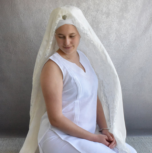 Woman wearing a white dress and veil against a plain background