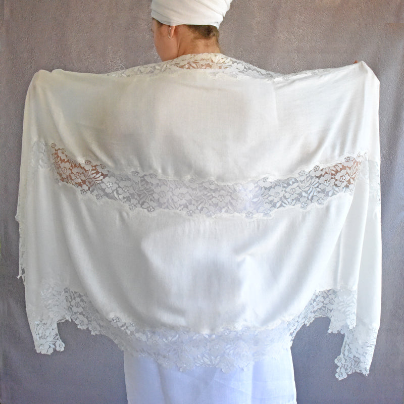 White lace shawl draped over a person against a plain background