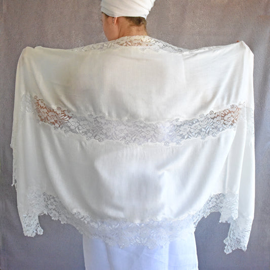 White lace shawl draped over a person against a plain background