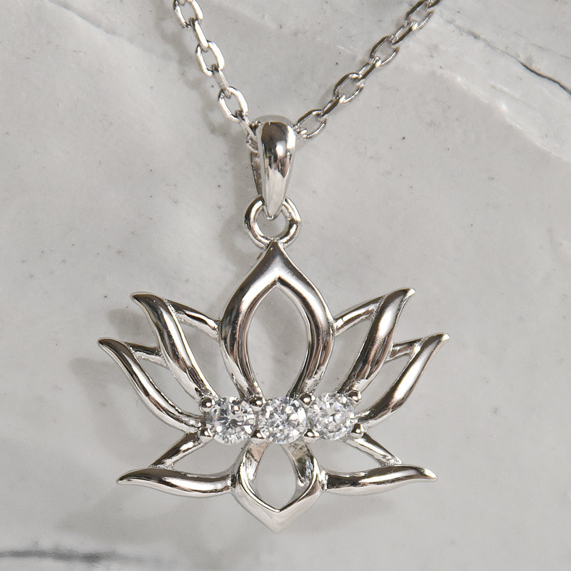 Silver lotus flower pendant with diamonds on a chain against a marble background