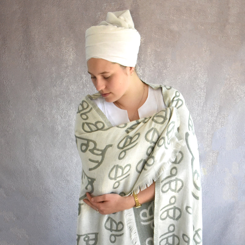 Person wearing a white headscarf and a patterned shawl against a gray background