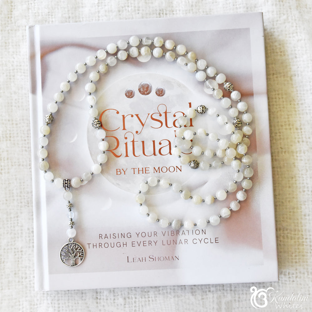 Pearly white mala necklace set on a book titled 'Crystal Rituals by the Moon' with a white background.