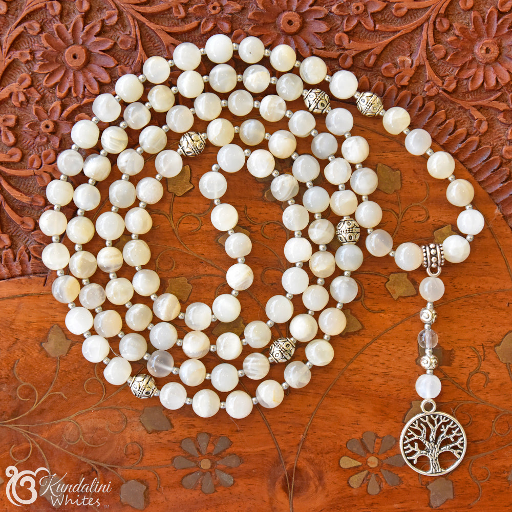 White beaded mala necklace with a tree of life pendant on a wooden surface