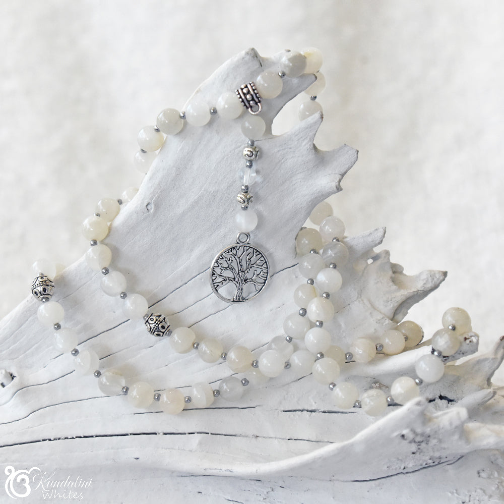 Mala necklace with off-white beads and silver tree of life pendant on a white surface
