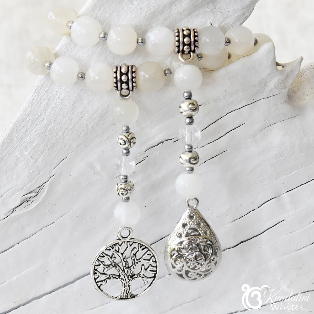 White beaded necklace with silver tree of life and teardrop pendants on a white wooden surface.