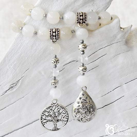 White beaded necklace with silver tree of life and teardrop pendants on a white wooden surface.