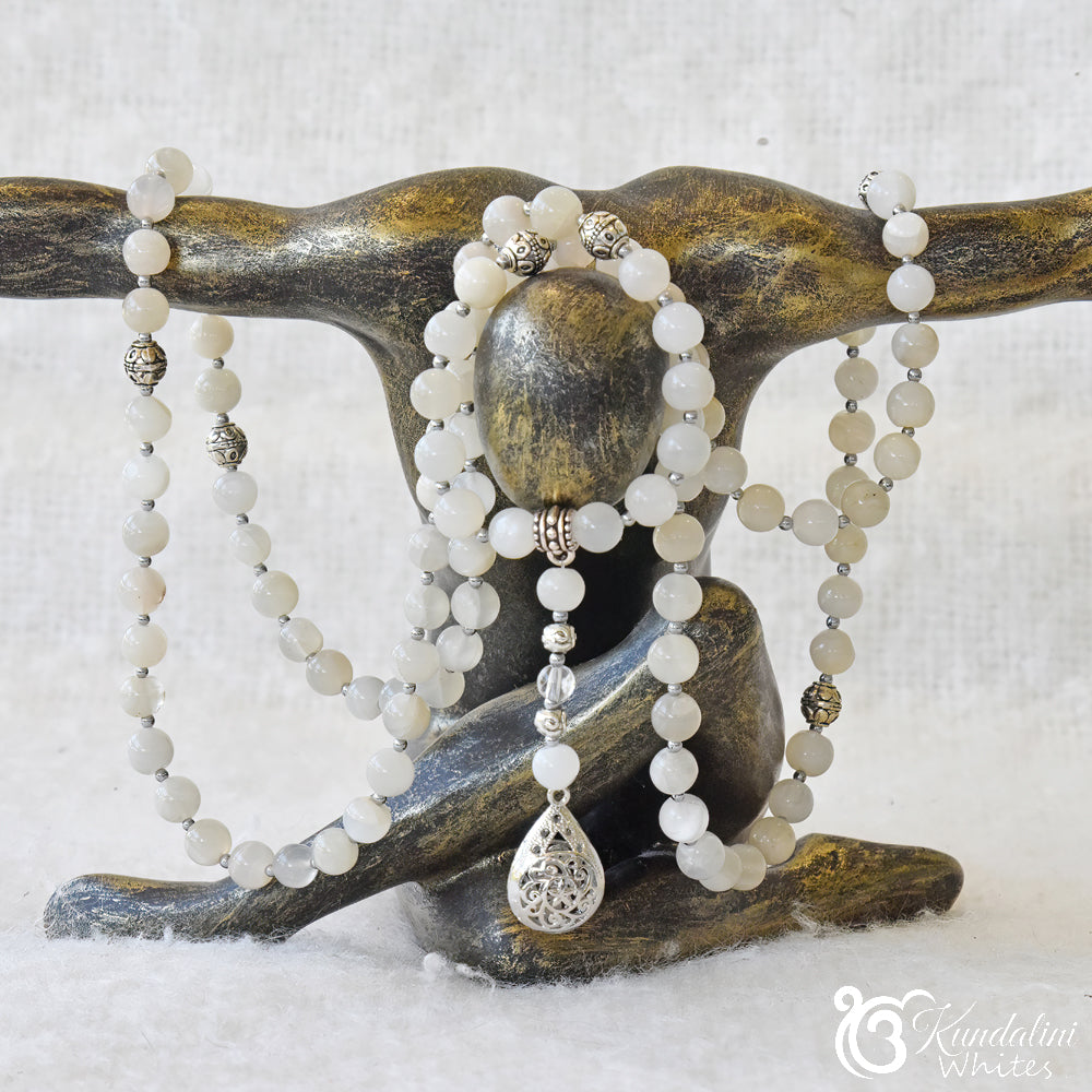 White beaded necklace with a silver pendant on a wooden stand.
