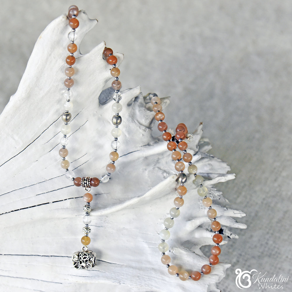 Beaded mala necklace with silver elephant pendant on a white branch with a gray background