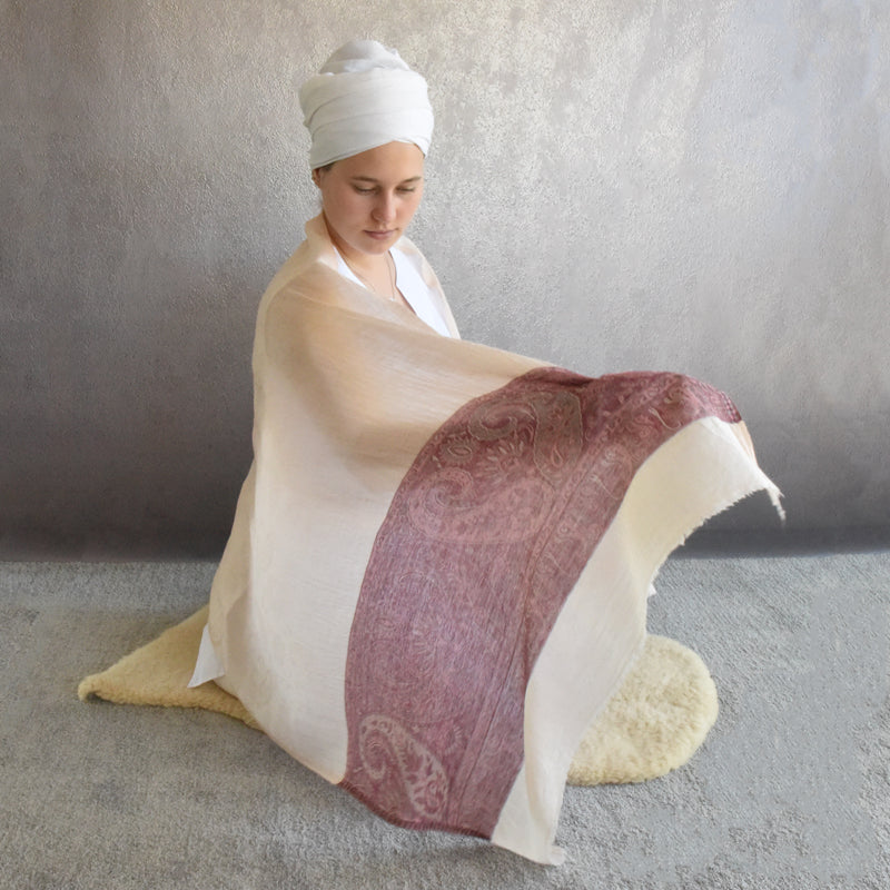 Woman sitting on a rug with a large white and red patterned shawl draped over her
