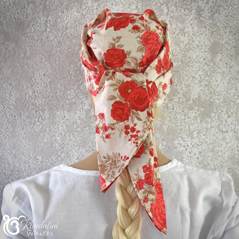 Person wearing a red and white floral headscarf with braided hair against a gray background