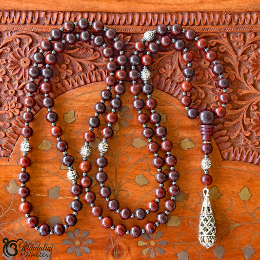 Wooden beaded mala with silver tassel on a wooden background