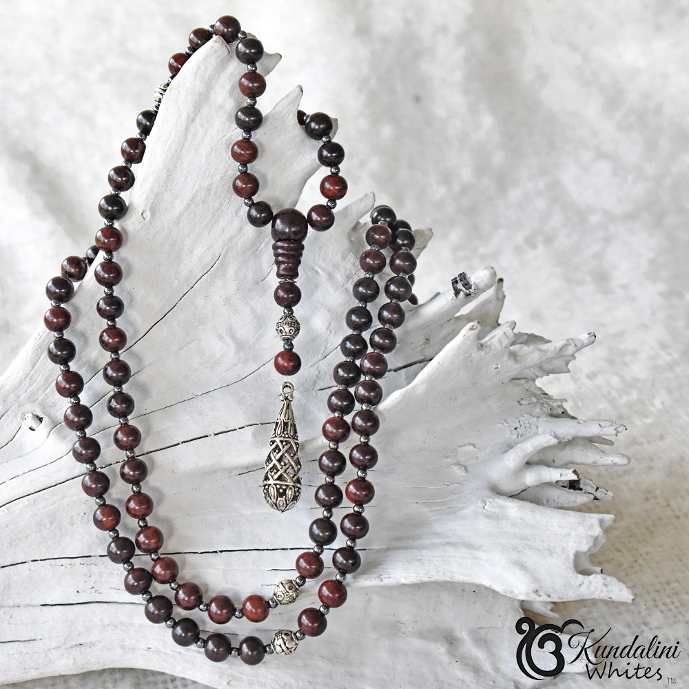 Wooden beaded mala with a silver pendant on a textured white background