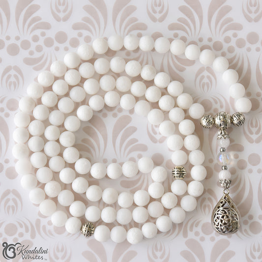 White beaded necklace with silver pendants on a patterned background