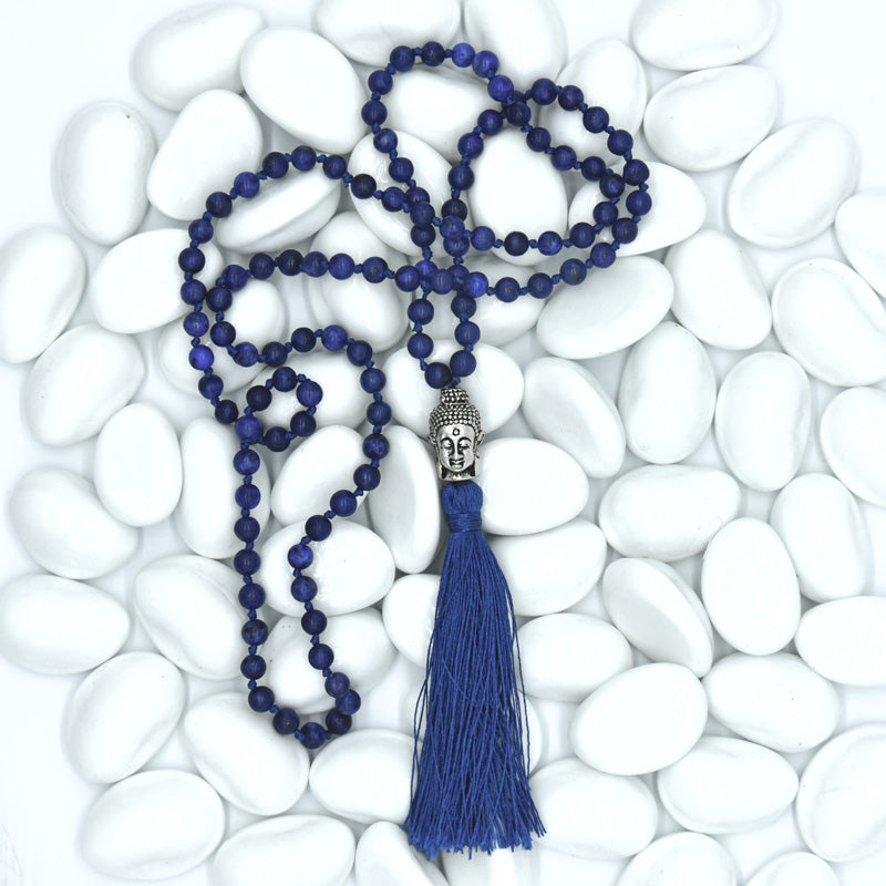 Blue beaded necklace with tassel on white pebbles