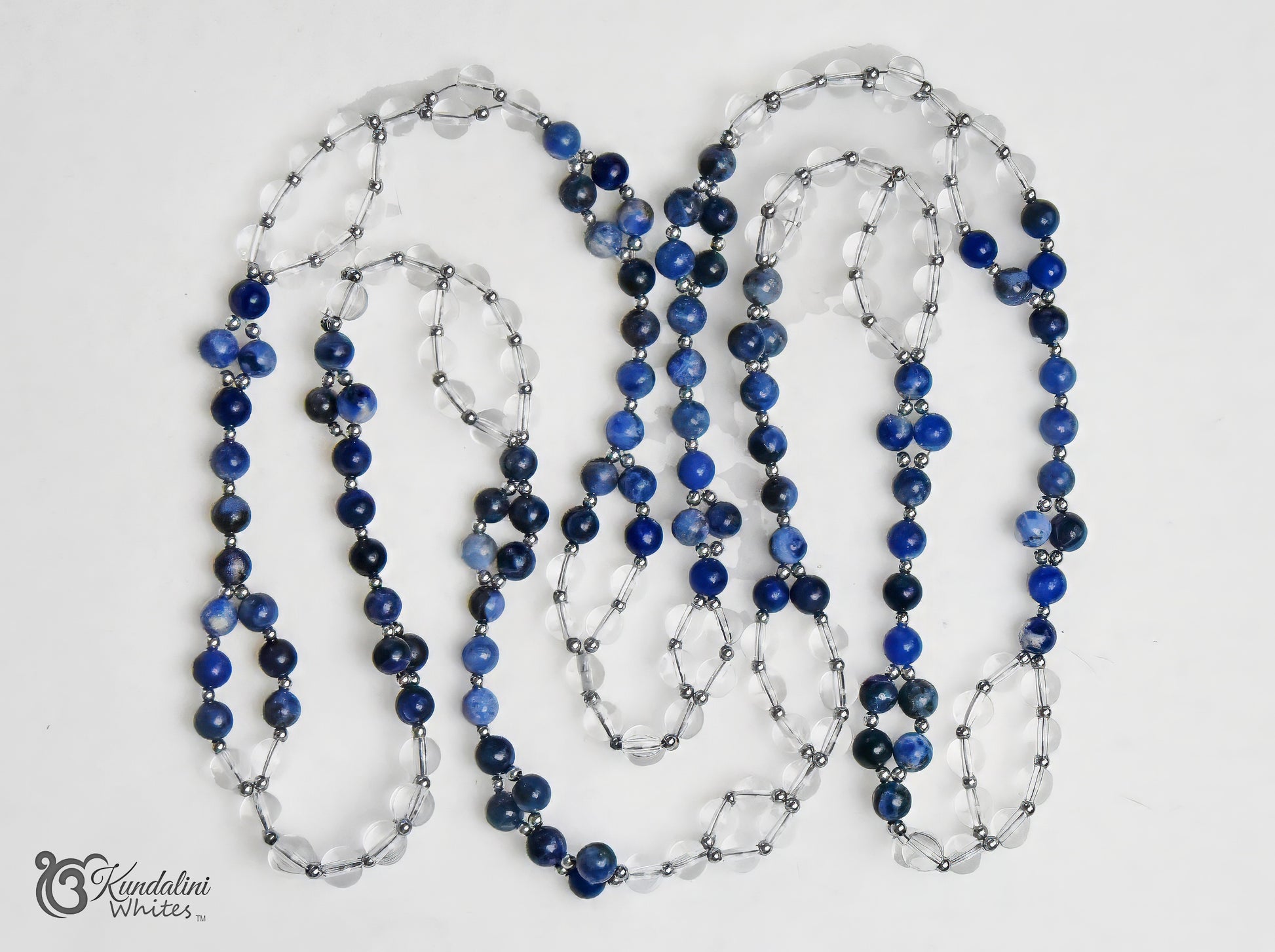 A Tantric necklace of sodalite and clear quartz beads, separated by small silver metallic spacers. The necklace is laid out in loops on a plain white background with a 'Kundalini Whites' watermark in the bottom-left corner.