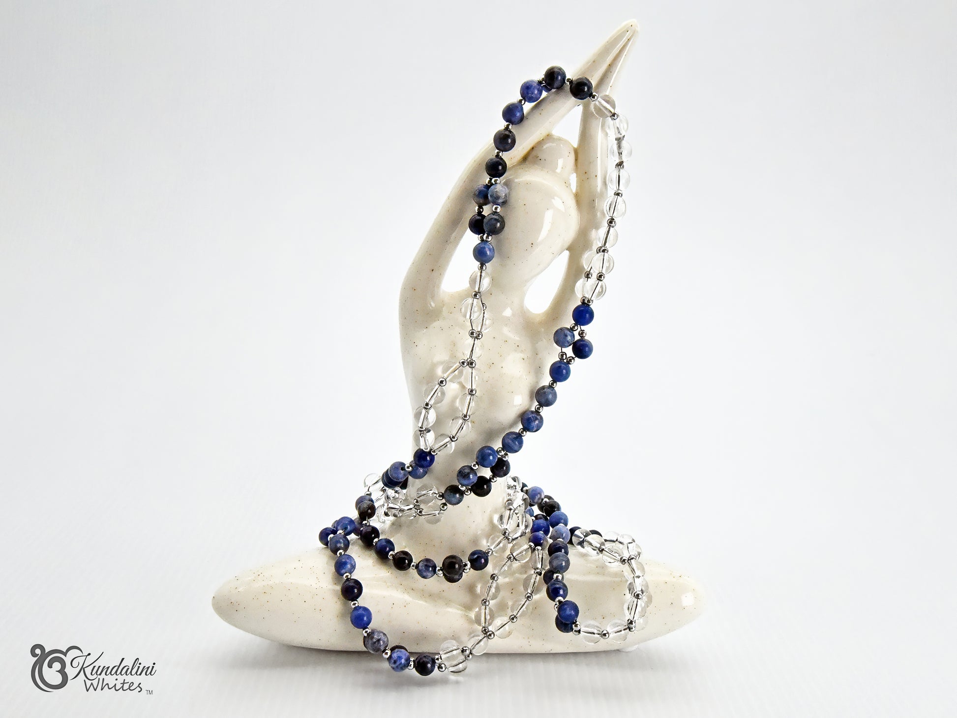 A sodalite and clear quartz Tantric Mala, accented with silver chain links, draped over a white ceramic figurine on a white background.