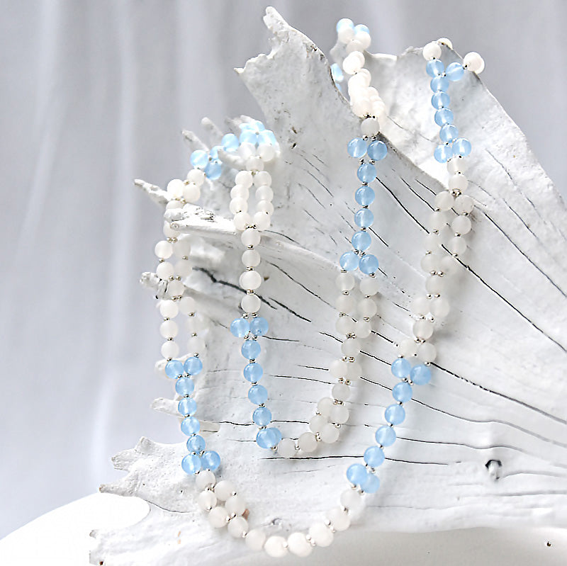 Two beaded necklaces with white and light blue beads on a white surface.