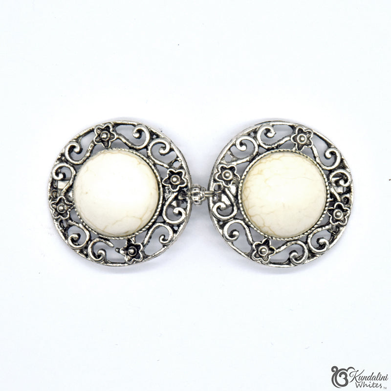 Shawl holder with white central stones and silver filigree designs on a white background.