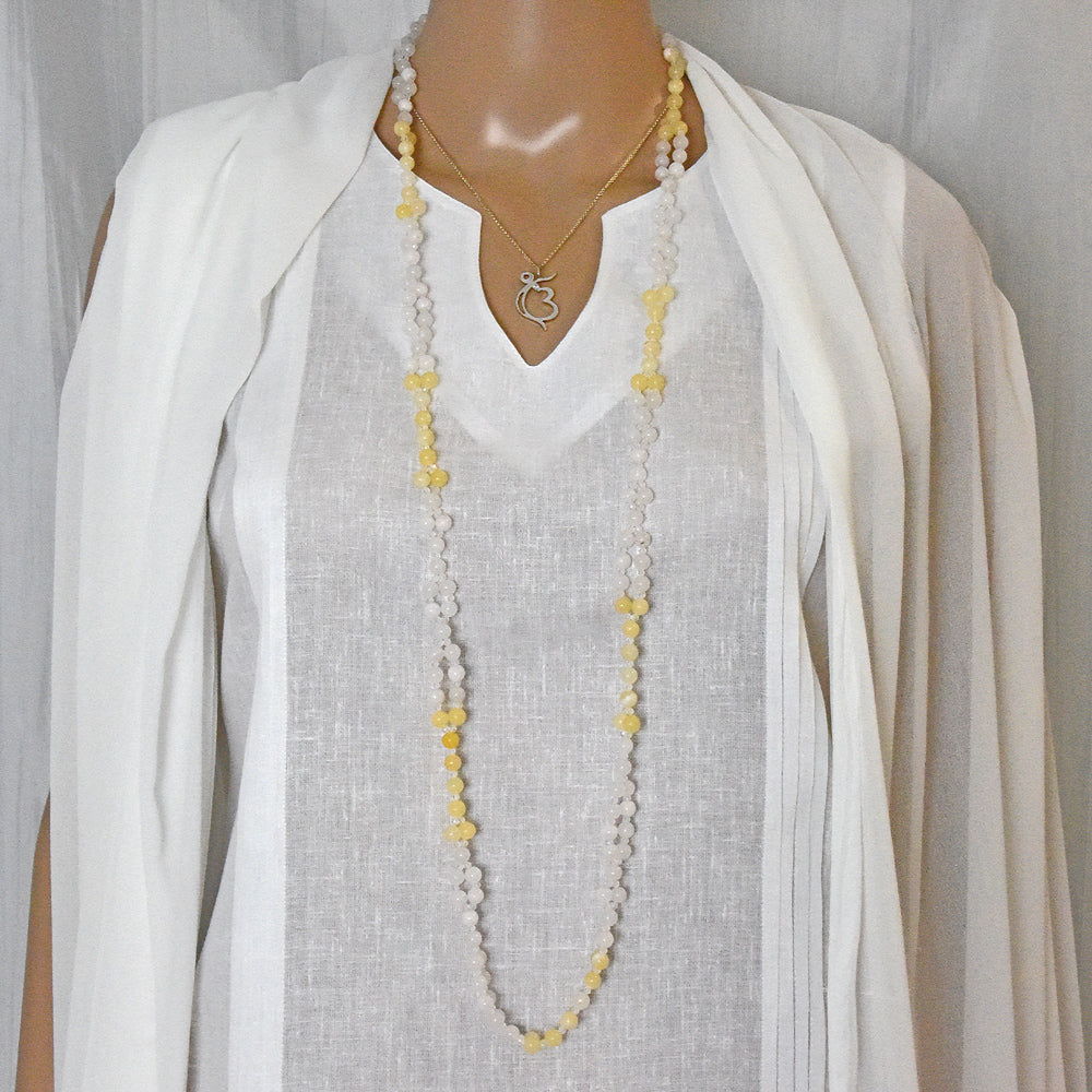 Mannequin wearing a long tantric necklace with a white outfit on a plain background