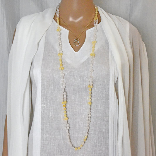 Mannequin wearing a long tantric necklace with a white outfit on a plain background