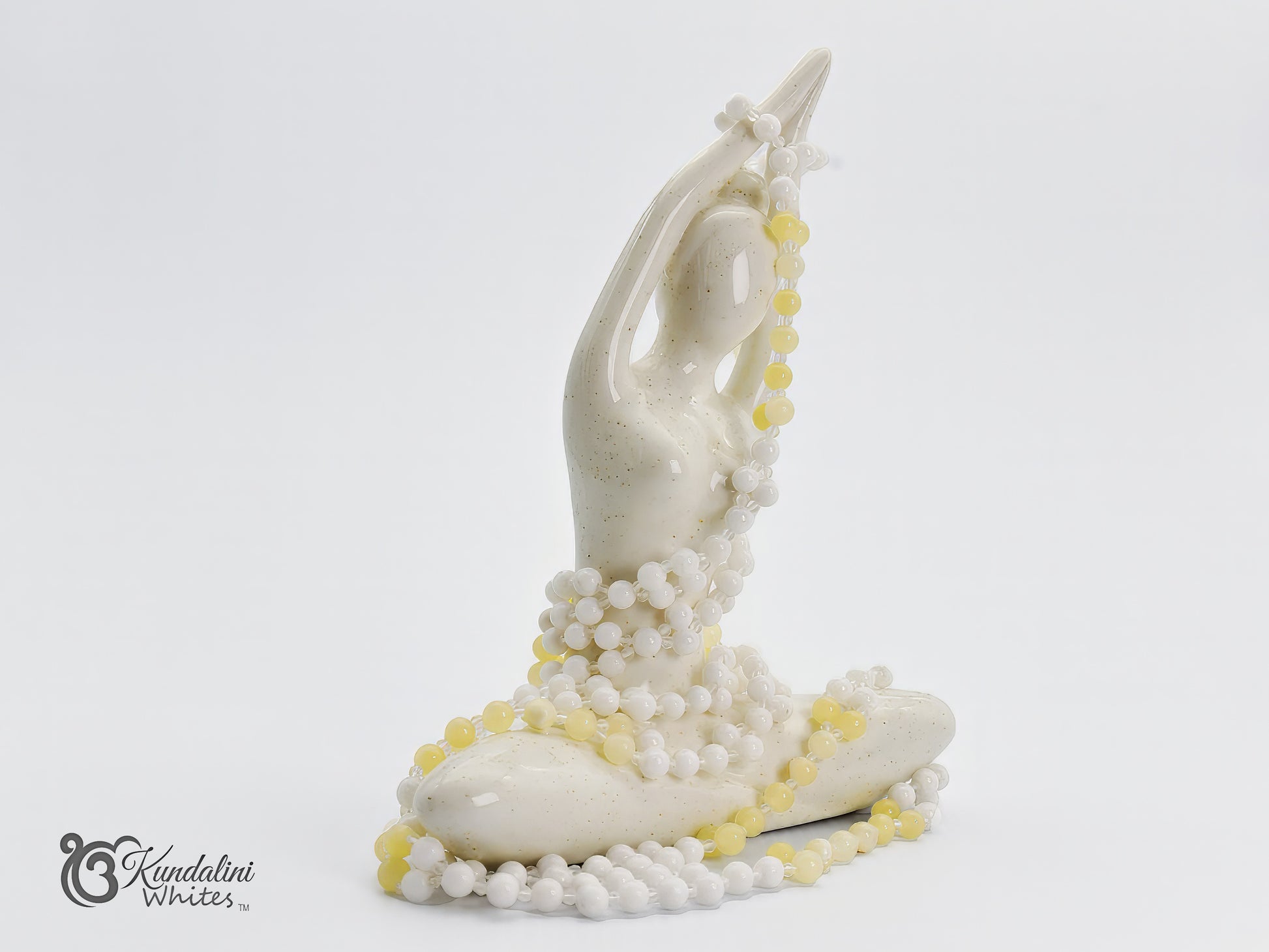 White sculpture of a figure with yellow and white tantric mala on a white background