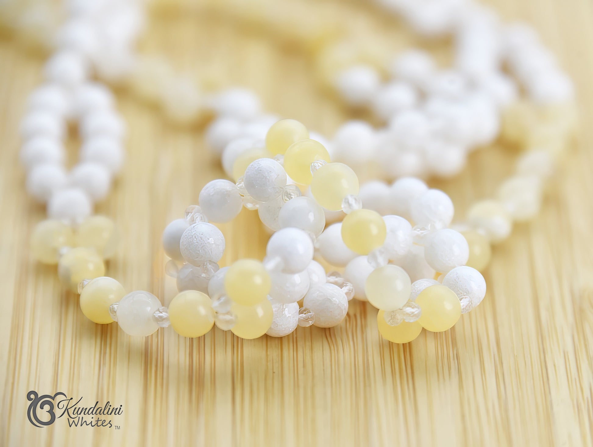 Necklace with white and yellow beads on a wooden surface, featuring the brand 'Kundalini Whites'.