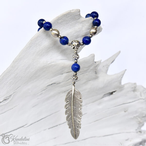 Close-up of 108 bead cobalt blue lapis lazuli mala with silver coloured embellishments wrapped around white timber