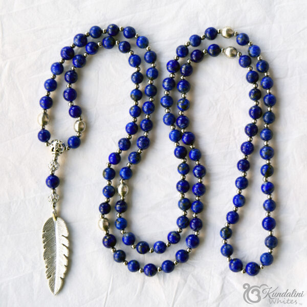 Cobalt blue lapis lazuli mala with silver coloured embellishments wrapped around white timber